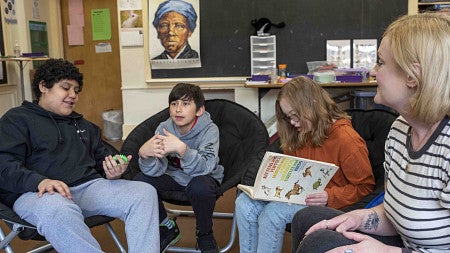 An educator talks with three students in a classroom