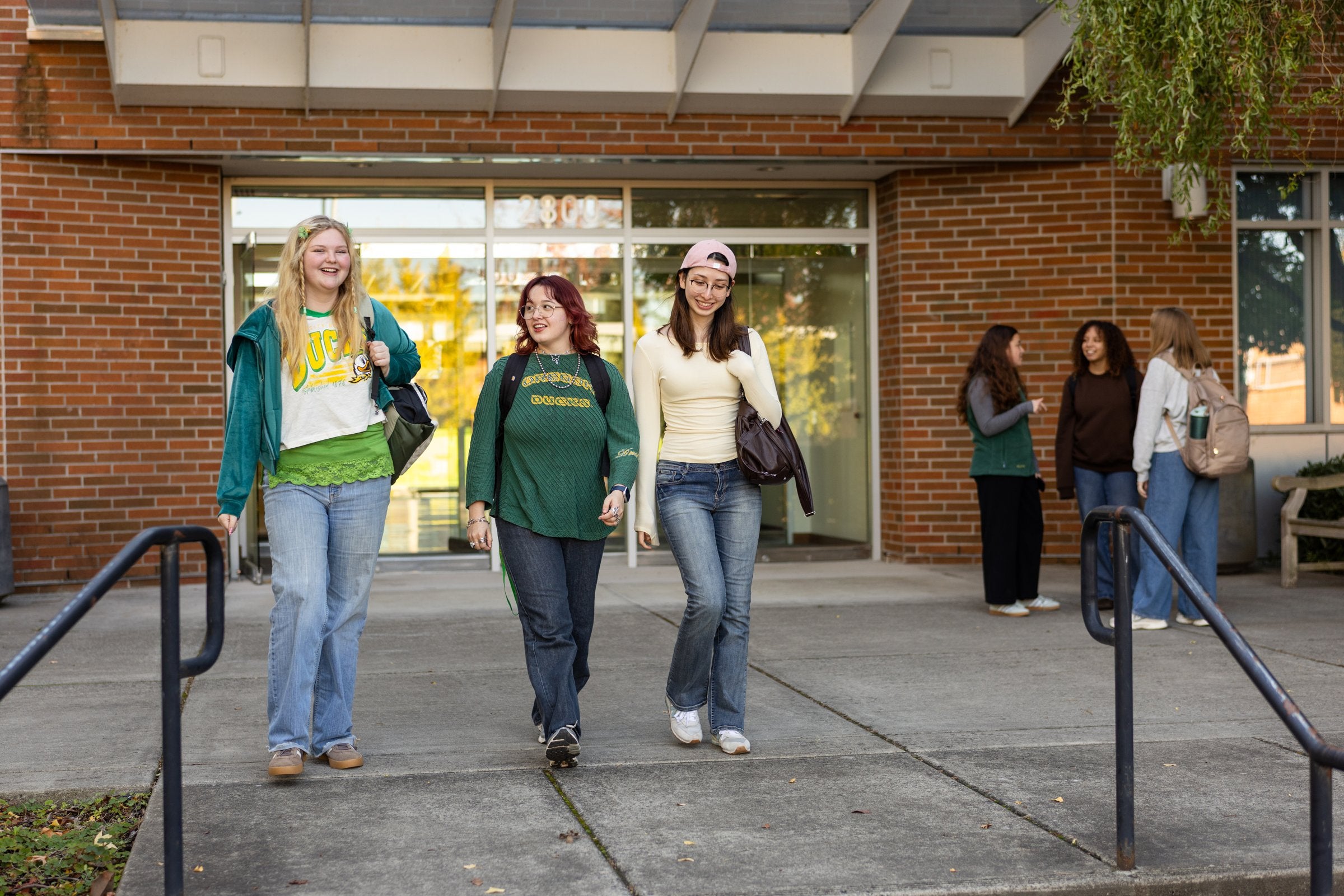 Three smiling University of Oregon students walk out of a campus building together