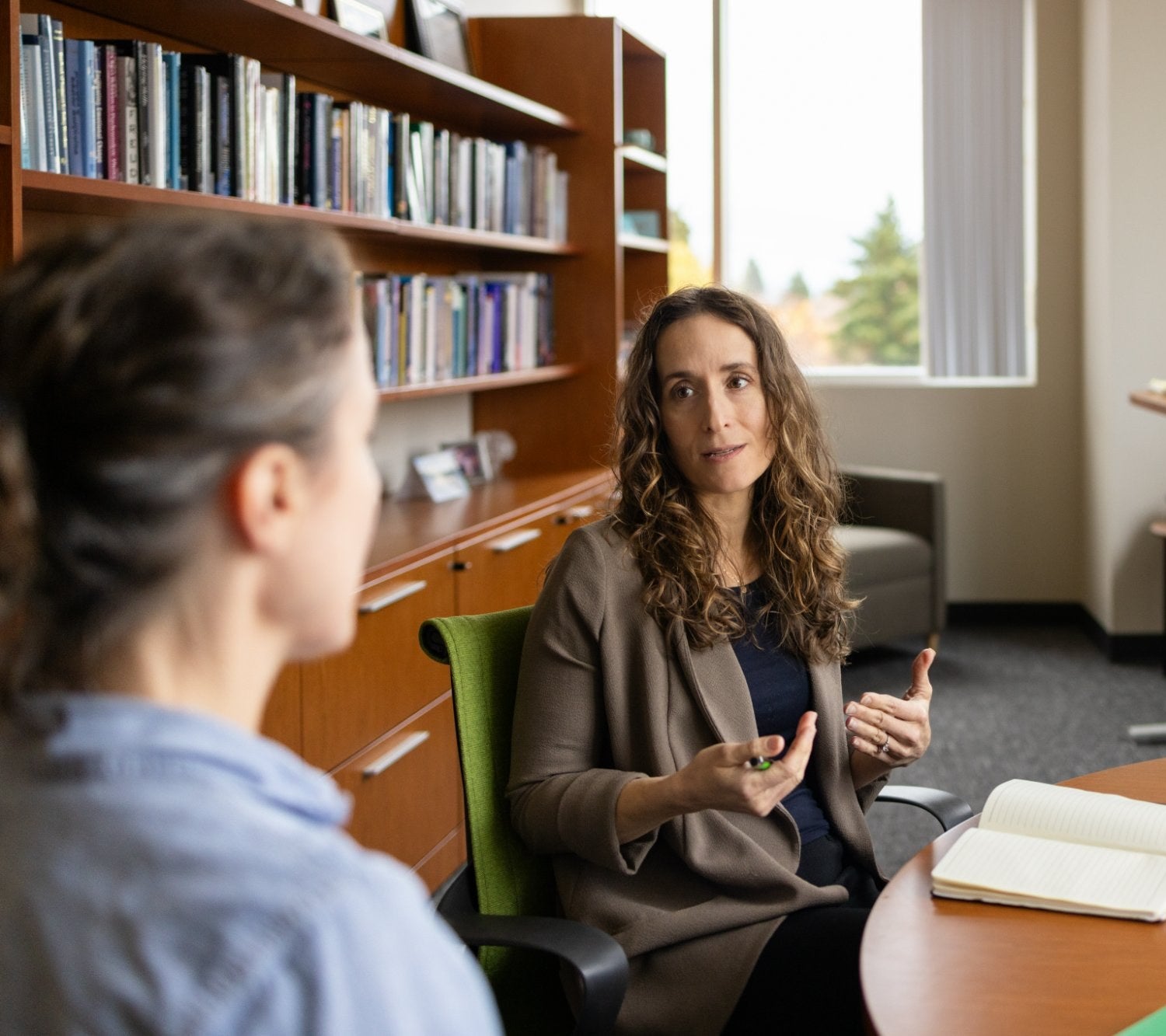 A Ballmer Institute leader speaks with a colleague across a table in an office lined with bookshelves