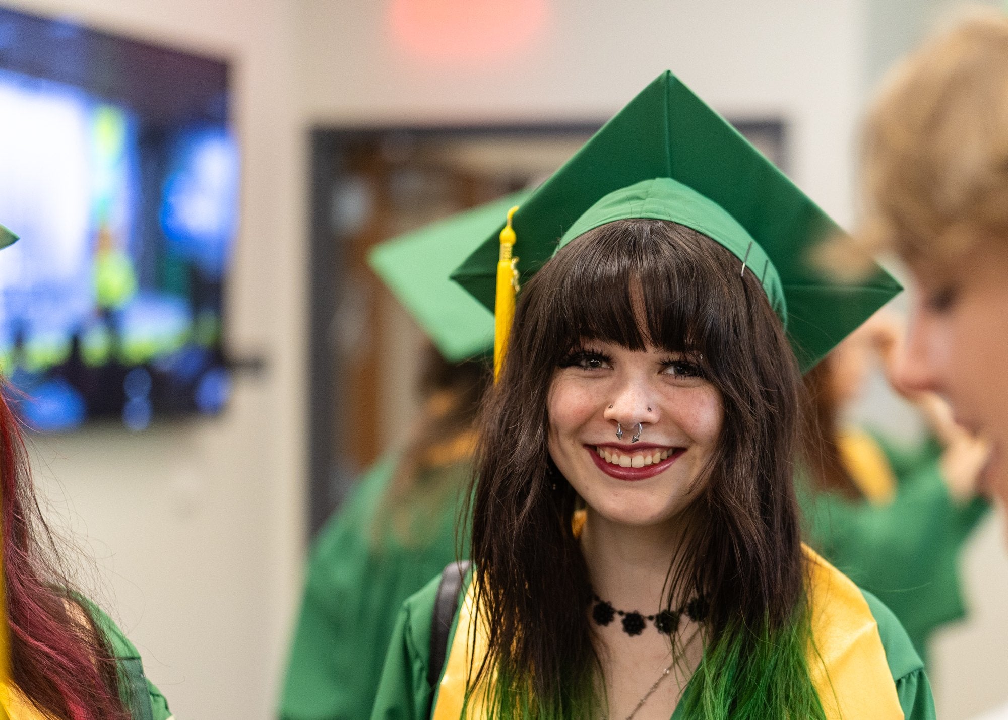 A smiling graduate in a green cap and gown and gold stole at commencement