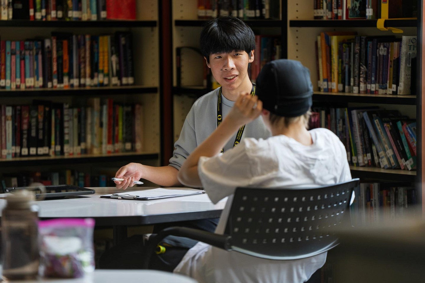 A Ballmer Institute student wearing a University of Oregon lanyard meets with a young person at a table in a school library.