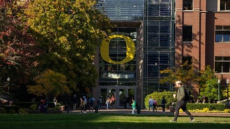 students walk across grass in front of a building at the University of Oregon