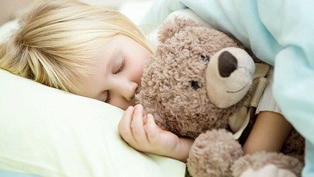 A sleeping child is shown hugging a teddy bear
