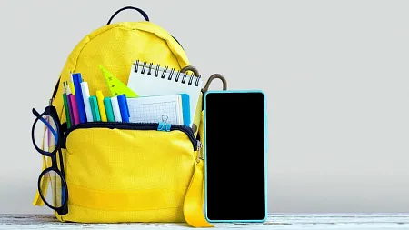 A backpack full of school supplies sits next to a cell phone