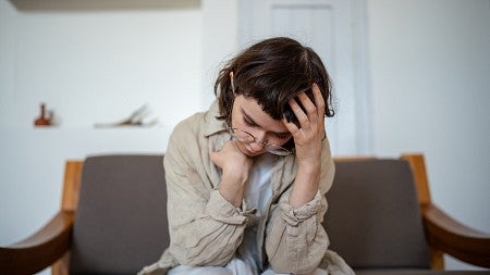  Young woman sitting on a couch, holding her head in her hand, looking distressed or thoughtful.