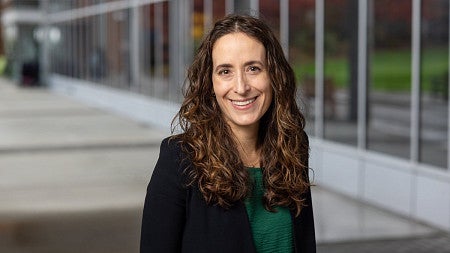 Dr. Katie McLaughlin, Executive Director of the Ballmer Institute for Children's Behavioral Health, smiling outdoors in front of a modern building on the University of Oregon Portland campus.