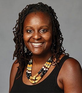 Headshot of a smiling woman, wearing a sleeveless black top, beaded necklace, and earrings, against a neutral background