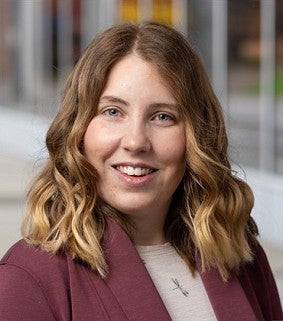 Person wearing a burgundy blazer over a light top, standing outdoors near a modern glass building.