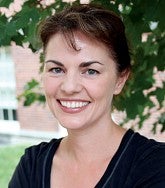 a woman smiles for a portrait standing outside in front of a tree