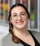 Han Padilla smiling, wearing glasses with a beaded eyeglass chain, a braid, and a gray cardigan over a black top