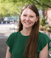 Mary Kuckertz smiling outdoors, with long reddish-brown hair and a green top.