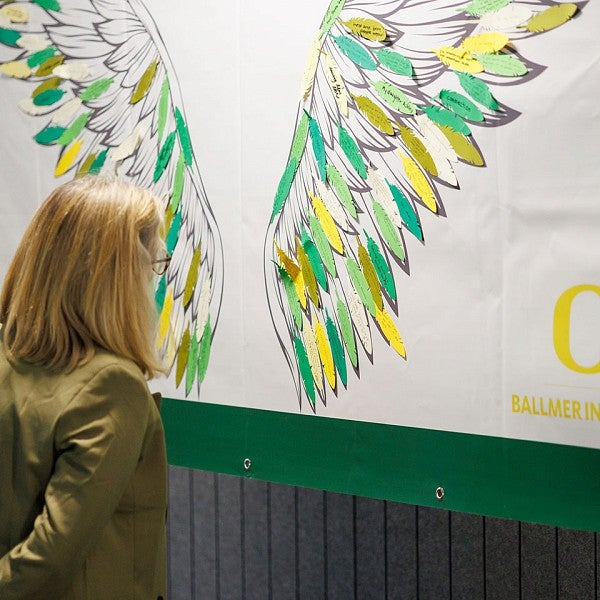 A woman reads notes written on paper shaped like feathers on a large illustration of wings 
